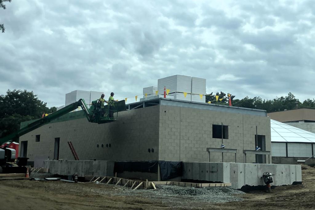 Roof construction on the tertiary building with construction workers accessing the building construction utilizing a lull
